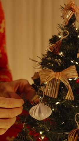 Close View of Woman Attaching Ornament to Lower Branch of Mini Christmas Tree Surrounded by Warm Holiday Decor.