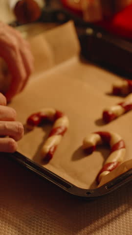 Woman Reaches Toward Tray with Shaped Candy Cane Cookies in Warm Light with Santa Hat Nearby.