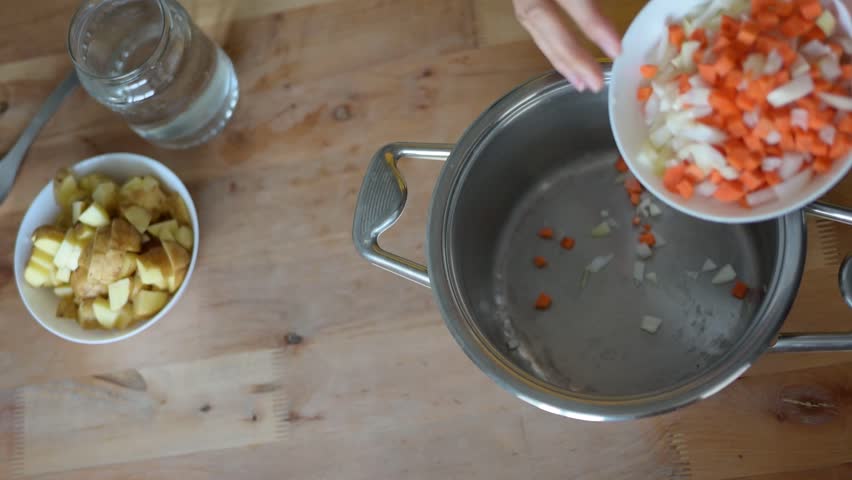 Chopped vegetables cascading from white bowl into stainless steel pot, alongside diced potatoes and water on video wooden rustic surface fullhd