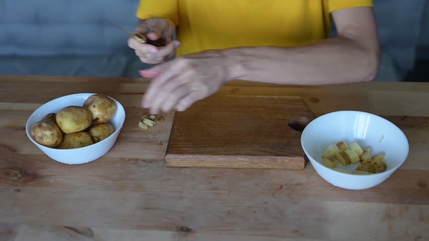 Hands peeling a potato over a wooden cutting board, with a bowl of potatoes an empty bowl nearby, ready fullhd food preparation video