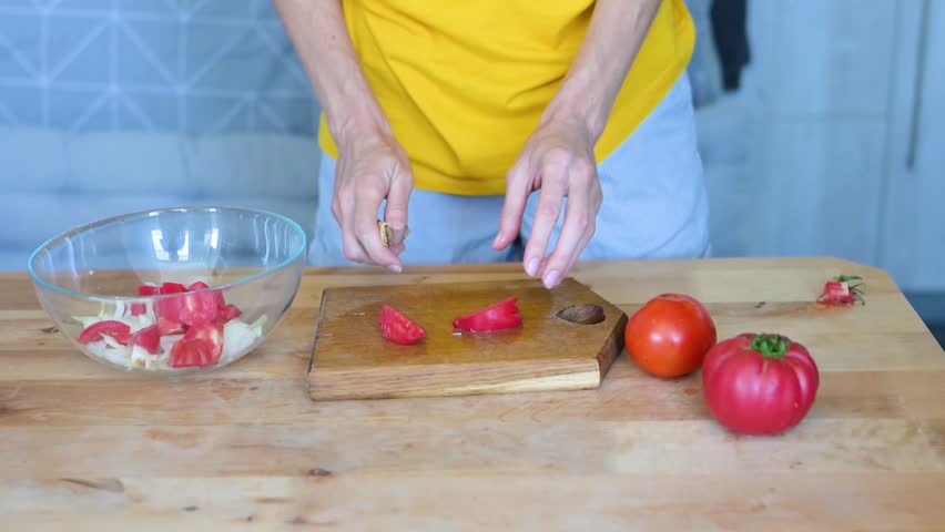 Knife slicing ripe tomatoes on rustic cutting board, preparing vibrant vegetable salad in transparent bowl video fullhd