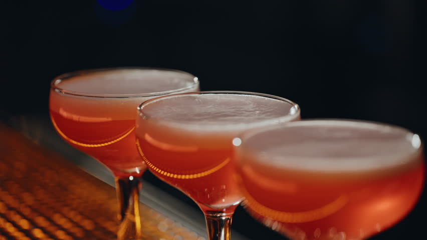 Creative barman splashing lemon juice on cocktail using lighter in night bar closeup. Unknown bartender hands adding sour ingredient to glasses drinks at bar counter. Professional preparing beverage.