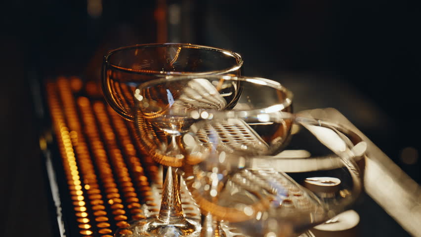 Hands pouring alcohol cocktail in elegant glasses standing at bar counter closeup. Unrecognizable bartender filling goblets with tasty drink. Foamy beverage flowing in transparent mugs in nightclub.