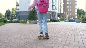 A girl in a pink jacket skateboards down a path towards school. She carries a pink backpack while navigating the smooth pavement in the early morning light, slow motion - Powered by Shutterstock - Get 15% off with code: PIKWIZARD15