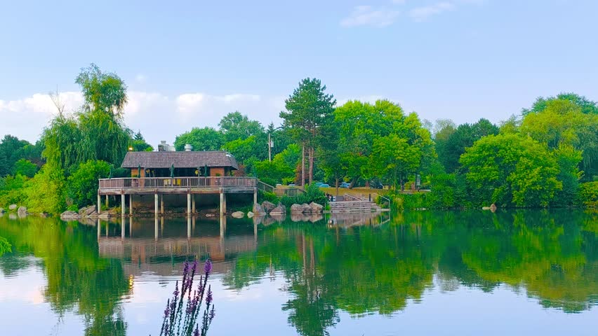 Cabin house surrounded by lush trees and foliage at an outdoor park by a lake, river, or pond in the wilderness. Forest, wildlife, fishing, reflections, serene nature landscape, scenic wallpaper.