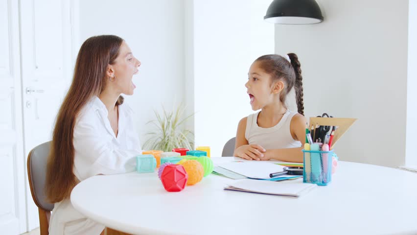 Speech therapist engages a young girl in playful language exercises at a bright, modern office during a therapy session