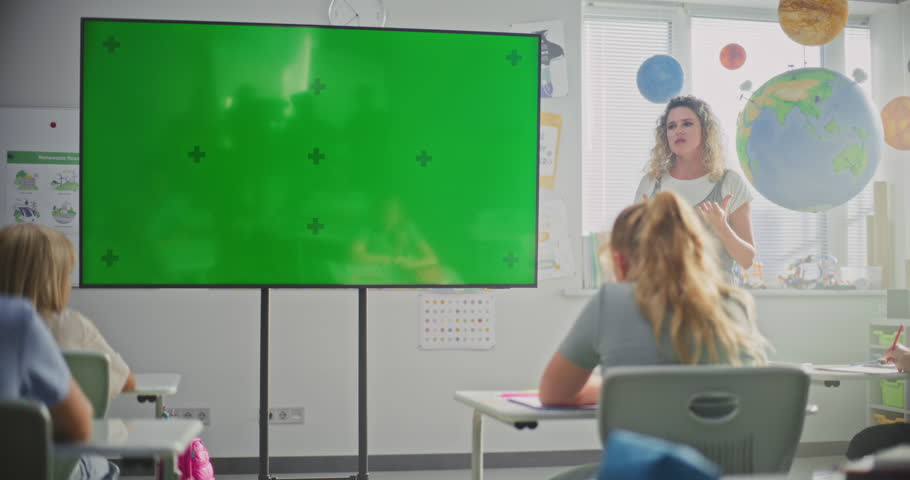 Modern Classroom: Female Teacher Teaching Primary School Children Using Large Digital Screen with Chromakey Mockup. Green Screen Placeholder for Educational Content or Interactive Visual Effects.