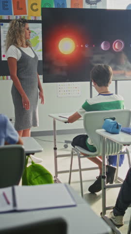 Elementary School Students Studying Basic Information About Solar System and Planets in Classroom. Female Teacher Educating Smart Kids During Astronomy Lesson Using Digital Screen. Vertical Shot.