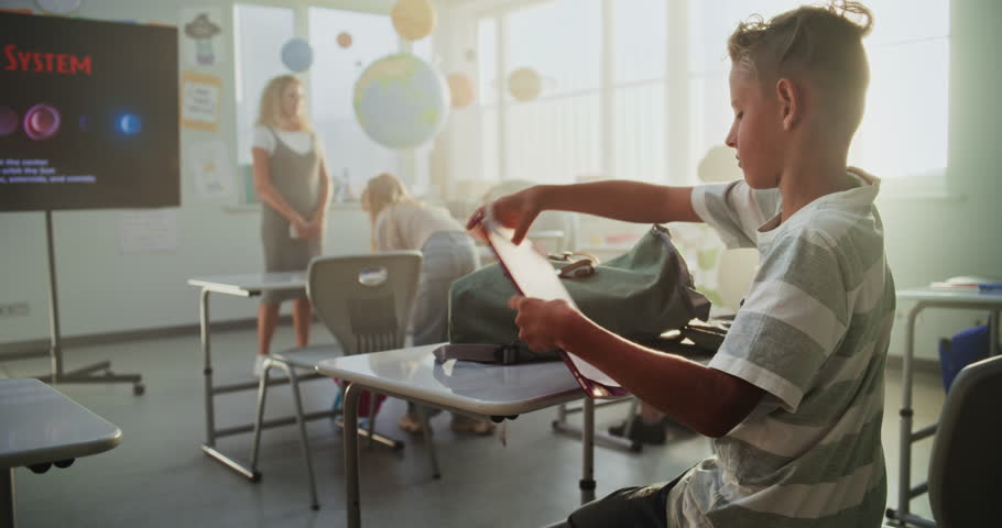 Elementary School Students Preparing for Class, Laying Out School Supplies on Desks in Modern Classroom. Female Teacher Greeting Group of Diverse Kids at the Beginning of Astronomy Lesson. Slow Motion