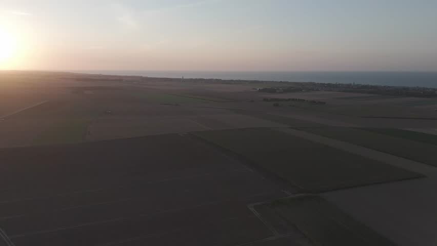 Aerial sunset over serene coastal farmlands.