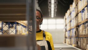 African american female reviewing merchandise data on files for logistics system, distribution hub with organizes shelving, for shipping protocols. Retail fulfillment and supply chain. Camera B. - Powered by Shutterstock - Get 15% off with code: PIKWIZARD15