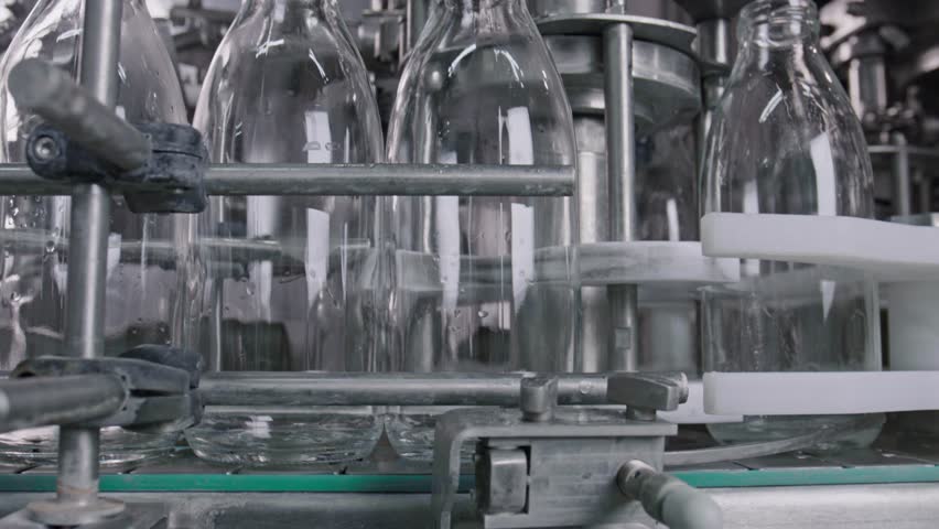 Empty glass bottles are moving on a conveyor belt through an industrial machinery, ready to be filled with milk, juice, or other beverages in a modern food processing facility