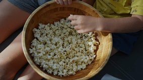 Children hands grabbing fresh popcorn from large wooden bowl during movie watching time at home on cozy sofa. Family snack time, siblings sharing food and comfortable home entertainment moments.  - Powered by Shutterstock - Get 15% off with code: PIKWIZARD15
