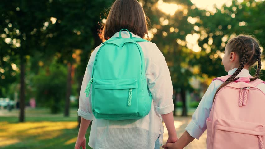Happy children walking down street to school. Children girls go with backpacks in park. Children go with school backpacks from school home. Girlfriends girls walk down street. Children's education