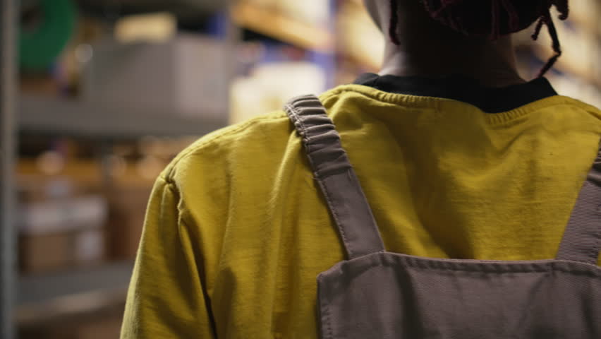 African american worker processing merchandise for business logistics system, busy warehouse space with industrial racks. Shipping protocols in online retail fulfillment center. Camera A.