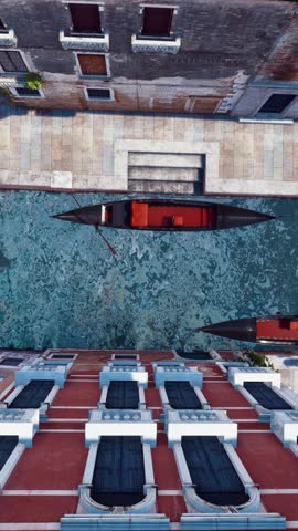 Straight overhead aerial shot of empty traditional venetian gondola boats and old stone bridge on narrow water canal in Venice, Italy. Top down view vertical video 3D animation rendered in 4K
