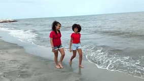 Two young girls, likely twin sisters, enjoy a relaxing walk along the beach, holding hands - Powered by Shutterstock - Get 15% off with code: PIKWIZARD15