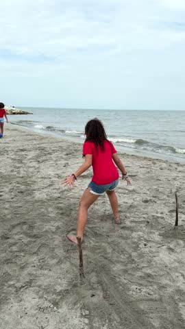 Two young girls enjoy a friendly game of beach soccer, running and kicking a blue ball on the sand