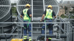 Two construction engineers in safety gear examine industrial HVAC units on rooftop, pointing and discussing project progress and setup - Powered by Shutterstock - Get 15% off with code: PIKWIZARD15