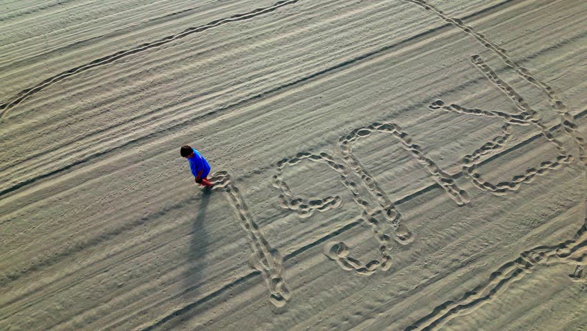 Playful Boy writes name with Bare Feet in Sandy Beach. High angle shot
