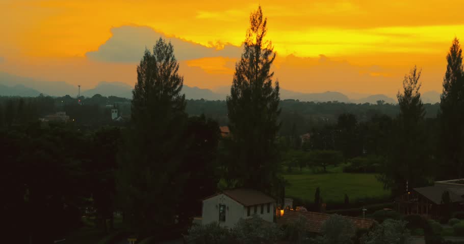 Sunset over tranquil rural landscape with silhouetted trees, vibrant orange sky, distant mountains. Peaceful countryside setting capturing natural beauty and serenity.