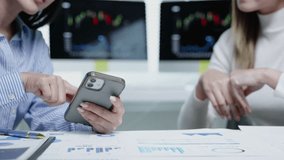 Colleagues review stock charts, discussing strategy while checking a smartphone in front of dual monitors during a finance meeting. - Powered by Shutterstock - Get 15% off with code: PIKWIZARD15