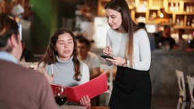 European woman holds a menu in her hands and orders food from a waitress in a restaurant. Smiling female waitress taking order in cozy restaurant with warm lighting. High quality 4k footage - Powered by Shutterstock - Get 15% off with code: PIKWIZARD15