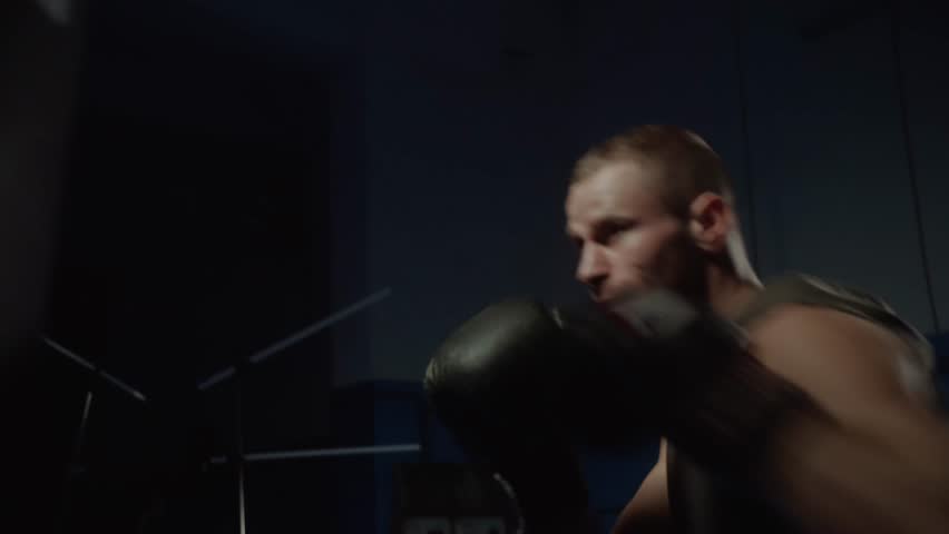 Boxer man hits boxing gloves punching bag in dark gym. Close up fighter workout. Male boxer exercising in dark. Kickboxer silhouette training. Slow motion 4k