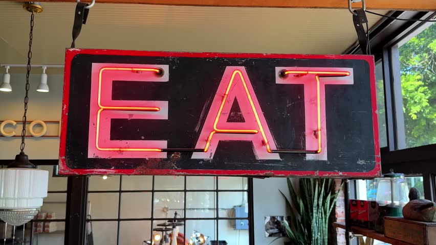 Classic Americana sign tube light that says "EAT" in glowing red letters at a diner or restaurant