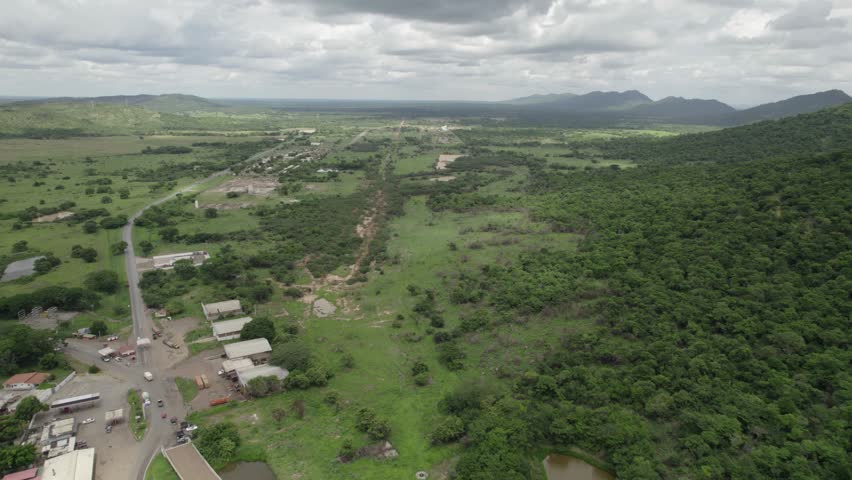 High aerial view of Dos Caminos town in Guárico, Venezuela, showing rural houses, rolling green hills, farmland, and lush countryside landscape.