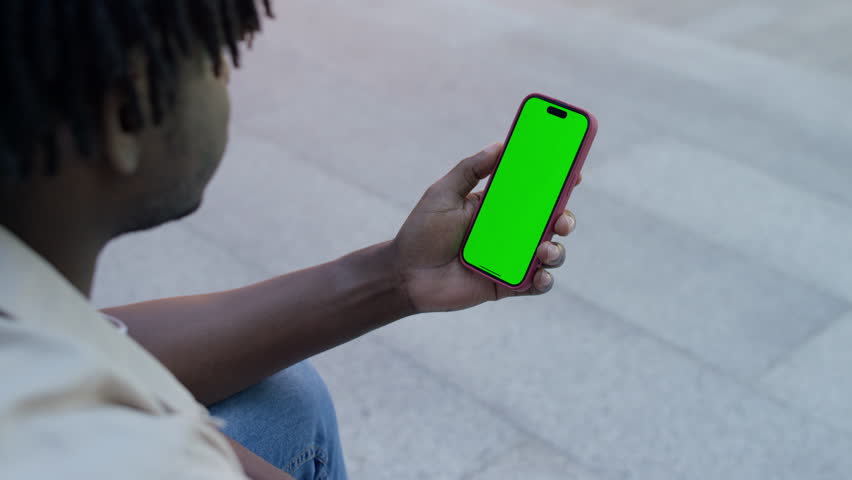 Close-up of a man hand holding a smartphone with a green screen mockup, suitable for app, website, or media display.