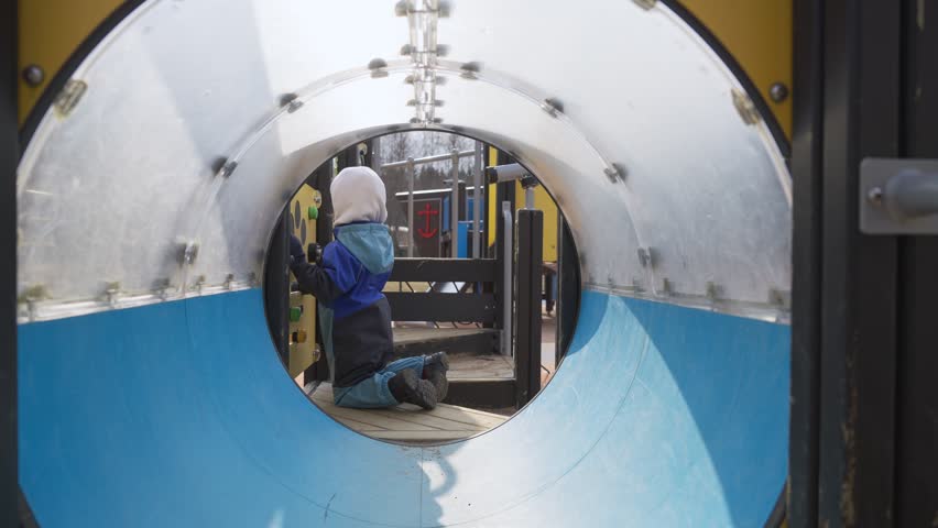 A smiling toddler in warm, comfortable seasonal clothing plays on a playground. Dressed for cold weather, the child explores and develops motor skills in a safe outdoor setting.