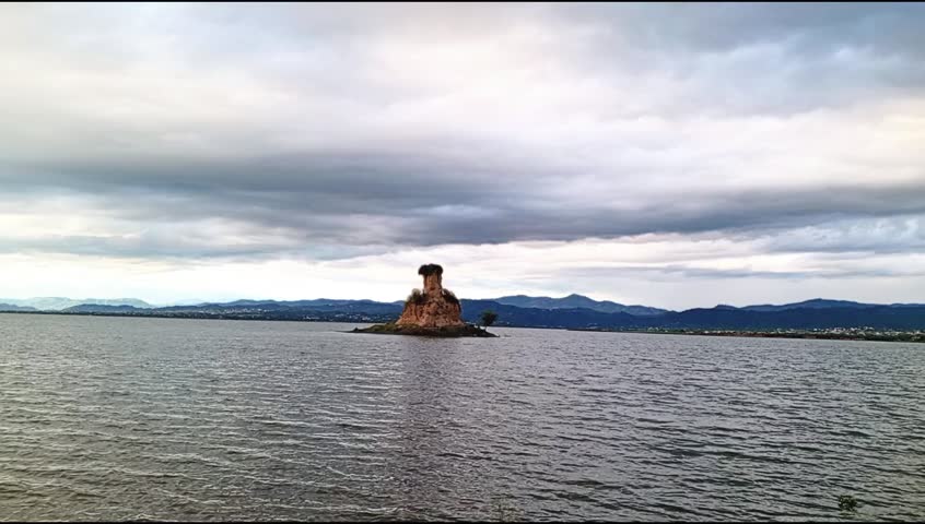 A breathtakingly beautiful and serene landscape panorama.The calm waters of the dam are full and perfectly reflect the sky. Behind it, a rustic earthen mound or hill stands under a dramatic canopy of 