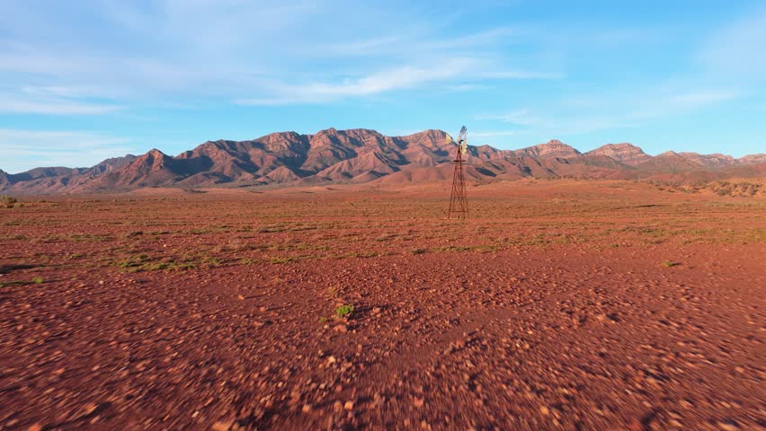 Fast low drone shot toward windmill across rugged red desert landscape, Flinders Ranges, South Australia