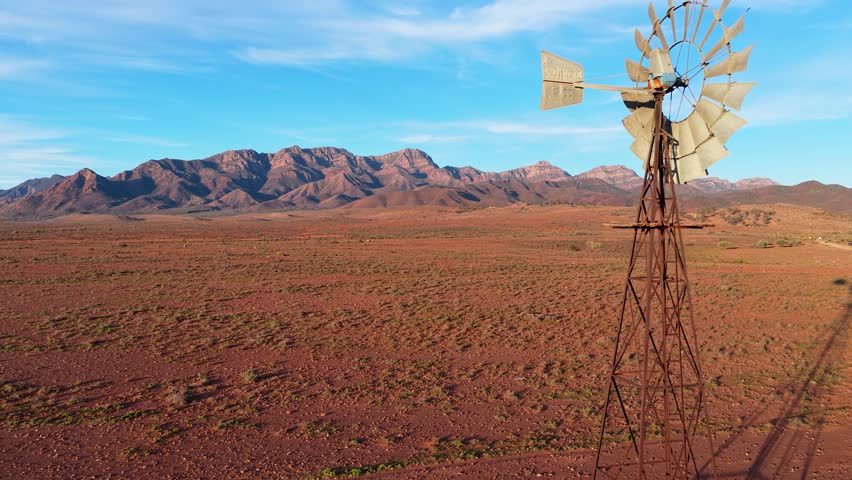 Slow smooth reverse shot of windmill, desert and Flinders Ranges mountains, South Australia