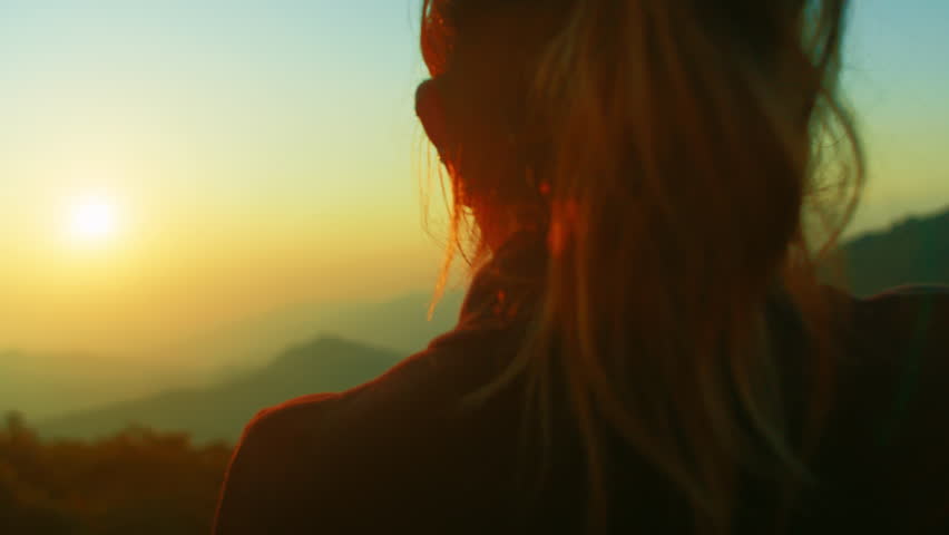 Woman from behind watching sunset on horizon with mountains valley view