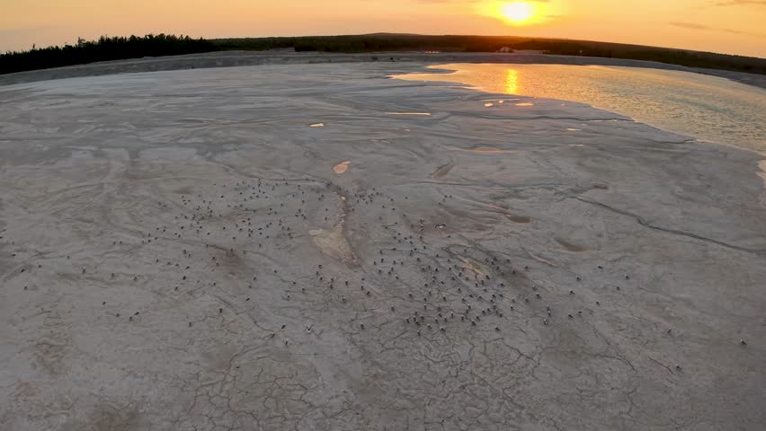 Aerial drone view of a barren sandy landscape with the sun setting over the horizon in the distance.