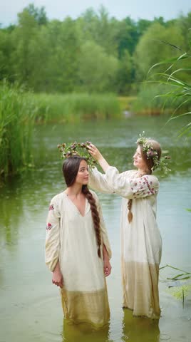 Video of Two young women in traditional ethnic costumes standing in the river during photoshoot