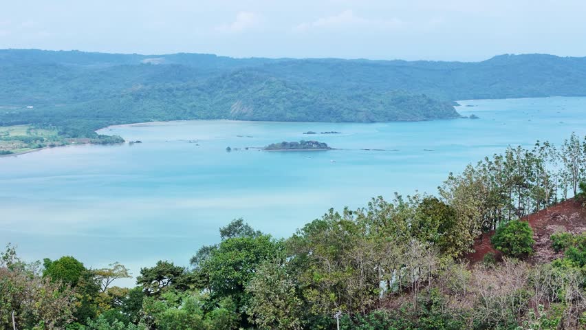 Stunning nature landscape with coastal green hills, blue ocean, and distant mountains. Summer holiday and travel background concept.