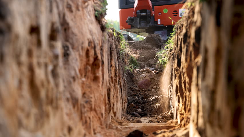 Mini excavator lifting soil from trench at construction site