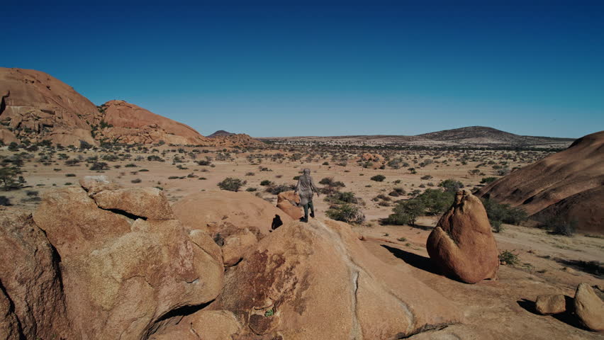 Man standing on rock in African desert while camera moves around him