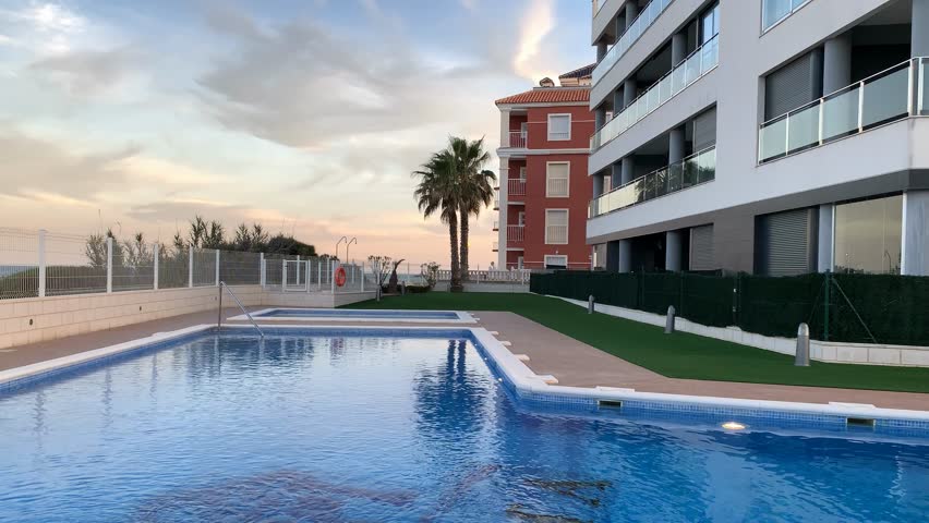 Apartment complex with outdoor swimming pool reflecting evening sky, ideal for vacation setting video