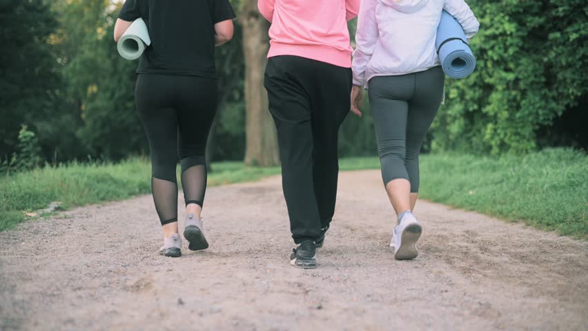 Three middle-aged women go to the park to do fitness. Rear view. Close up of legs.