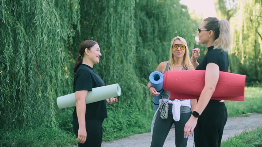 Three middle-aged women hug after practicing yoga together in a park.