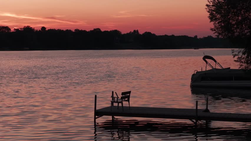 Low close-up aerial shot of a bench at the end of a dock on a Minnesota lake during sunset. 4K