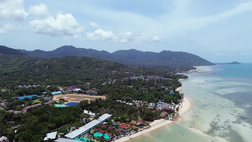 Aerial footage of Thong Sala Beach with a wide sandy shoreline, turquoise sea and lush tropical scenery on Koh Phangan island, Thailand.