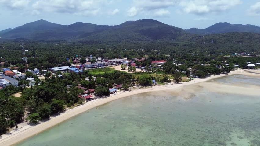 Aerial footage of Thong Sala Beach with a wide sandy shoreline, turquoise sea and lush tropical scenery on Koh Phangan island, Thailand.