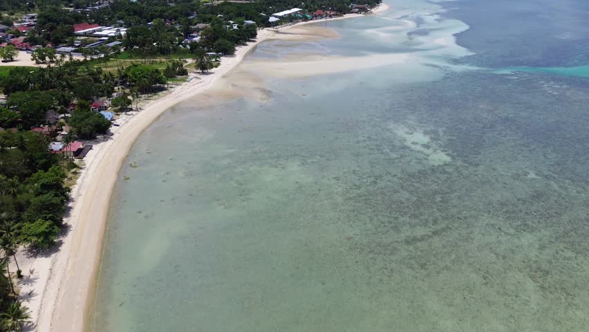 Aerial footage of Thong Sala Beach with a wide sandy shoreline, turquoise sea and lush tropical scenery on Koh Phangan island, Thailand.