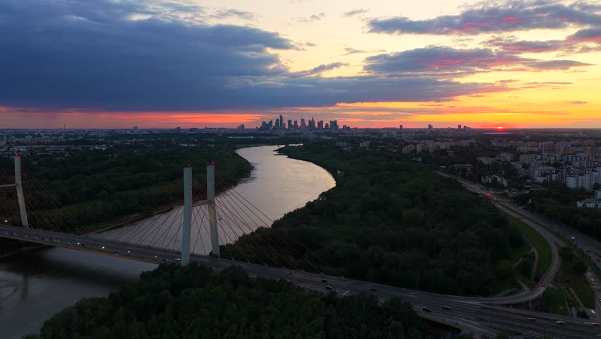 Aerial establishing shot of tranquil Vistula River, driving cars on Main Street in goclaw district of Warsaw. Sunrise in the morning. Wide shot. Skyline of Warsaw downtown in distance.