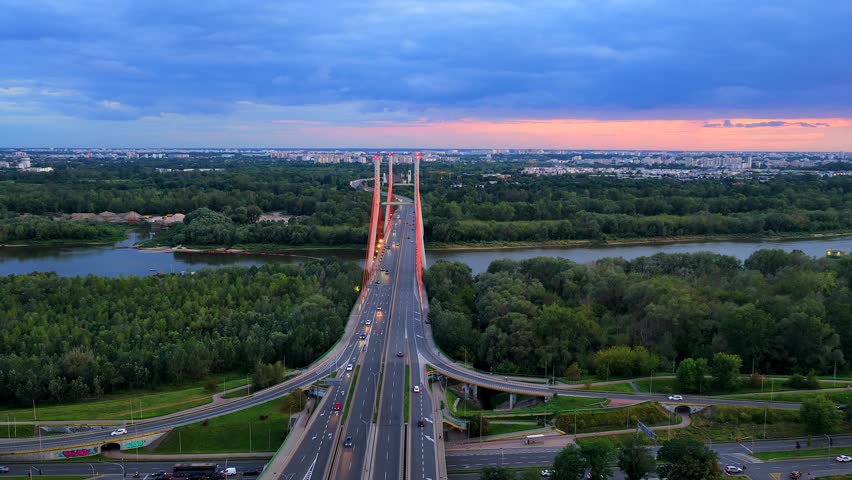 Aerial wide shot of traffic scene on Siekierkowski bridge and Siekierki coal power in background. Dusk scene in suburb of warsaw, Poland. Orbit shot. Vistula river in green landscape.